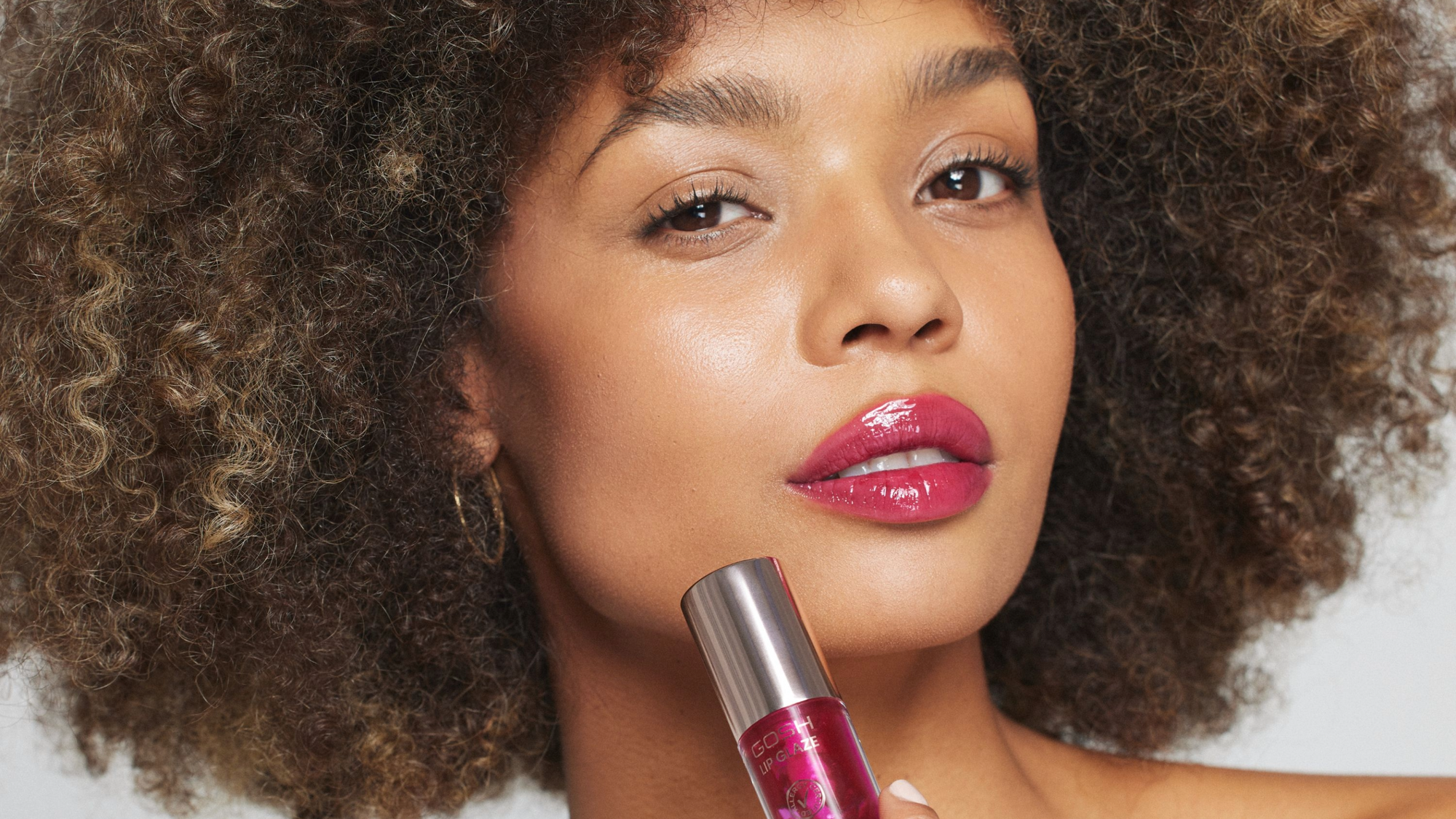 Woman displaying her cherry red lip style while holding a lip oil bottle