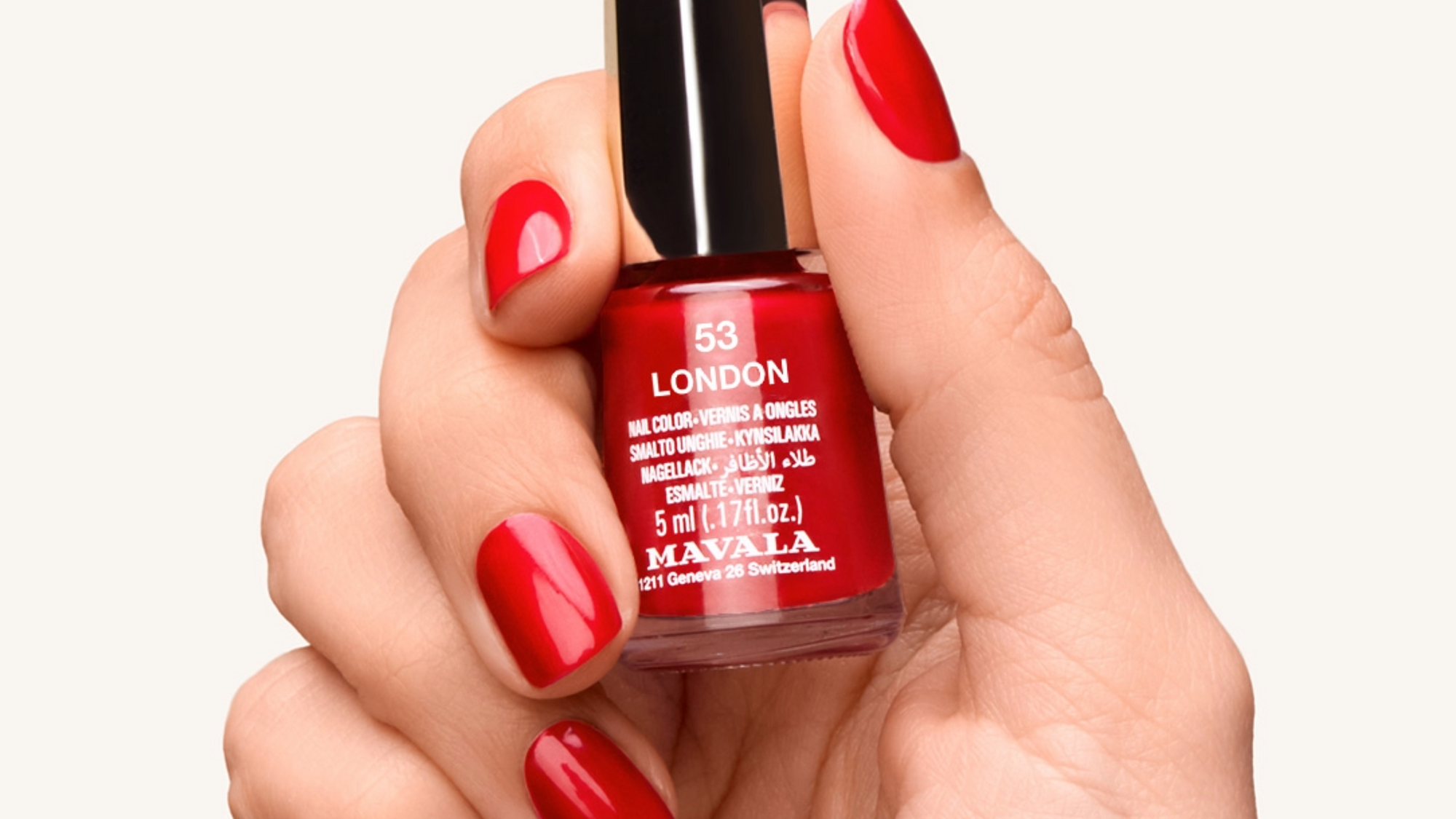 Kynsilakat: Naisen käsi jossa punaista kynsilakkaa ja Mavala 53 London kynsilakkapullo