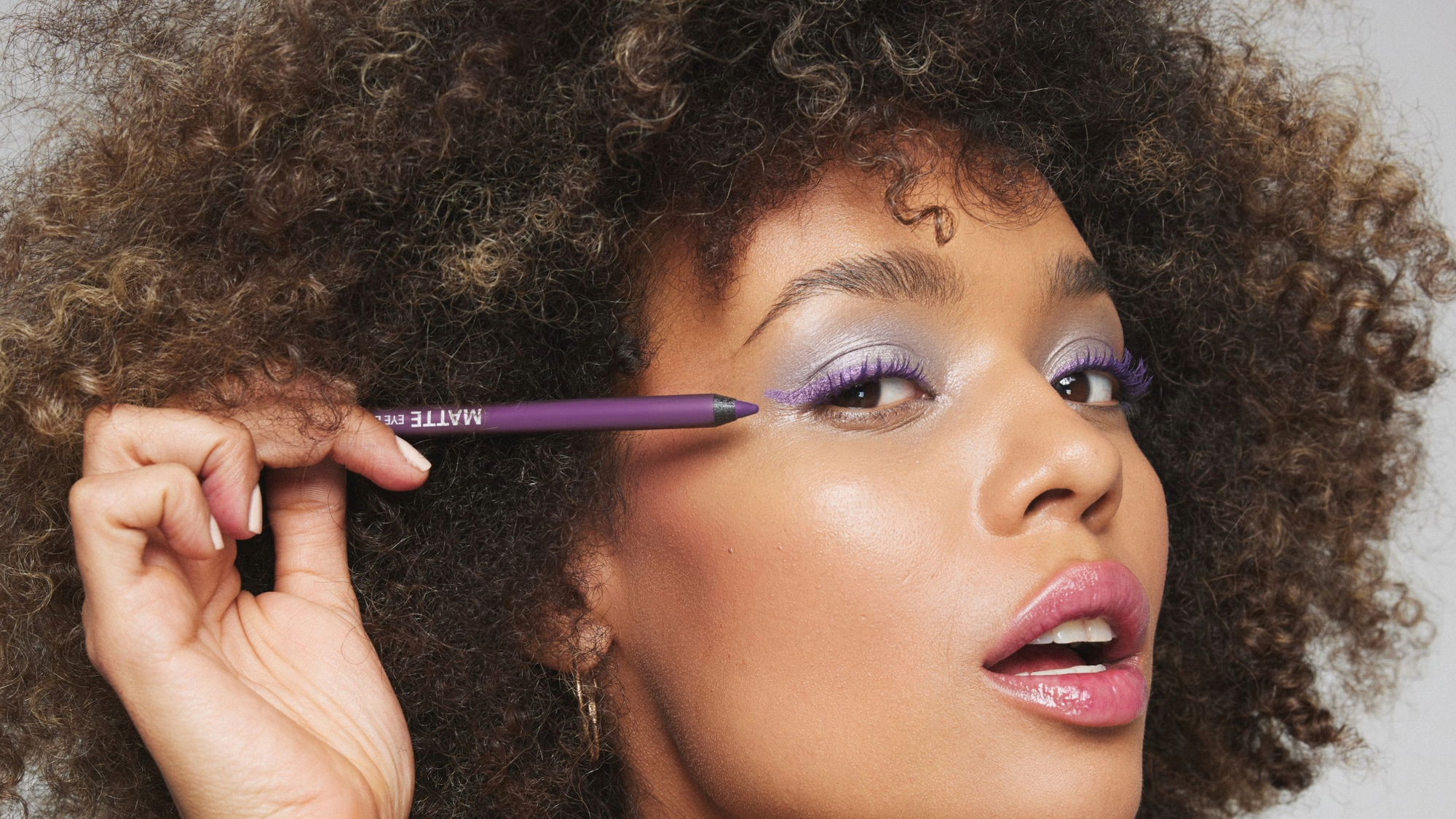 Silmämeikit: Naisen meikatut kasvot ja pitää käsissään liilaa silmänrajauskynää