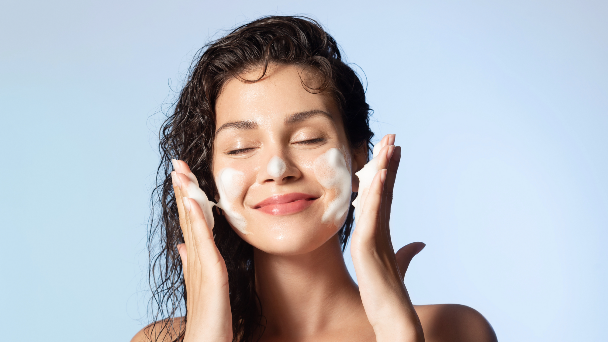 Hymyilevä nainen levittää kasvojen puhdistustuotetta poskilleen