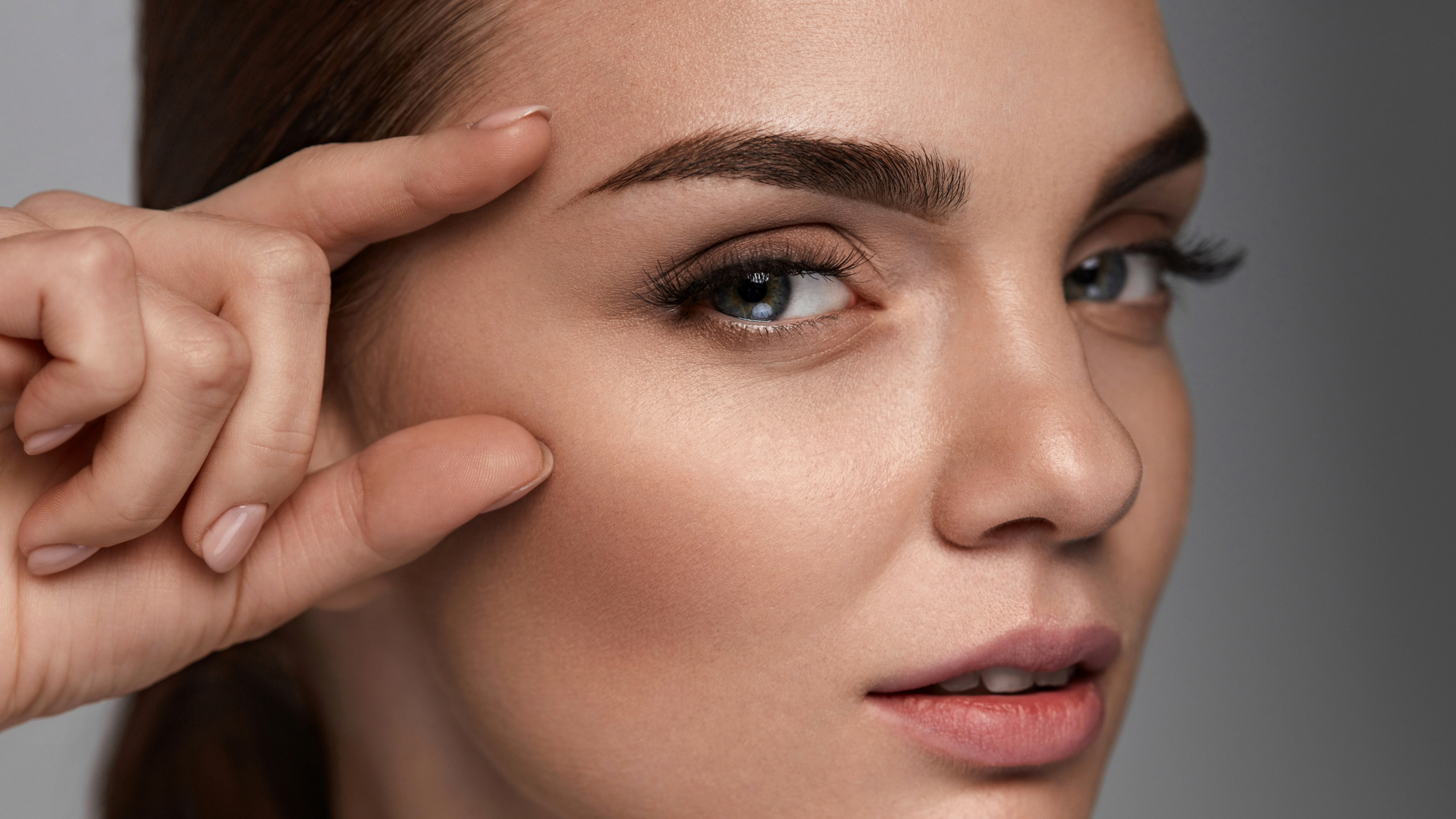 Lähikuvassa naisen kasvot ja sormet, jotka osoittaa kevyesti kulmakarvoihin