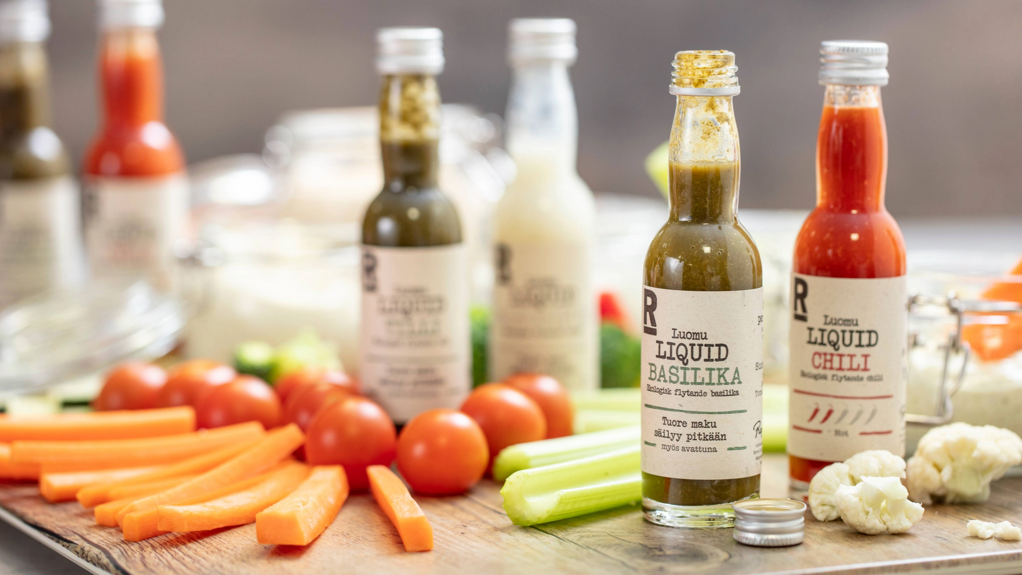Rajamäen Liquid Basilika ja  Liquid Chili pullot pöydällä kasvisten kanssa